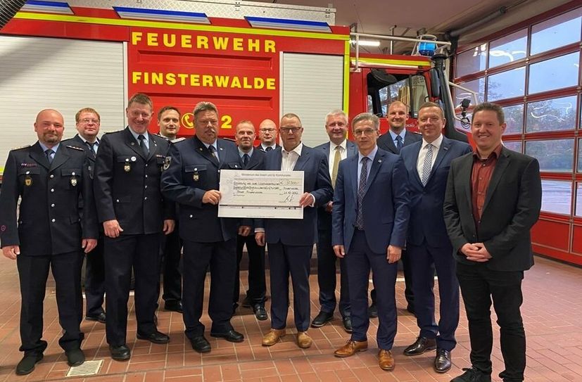 Stadtbrandmeister Michael Kamenz nimmt stellvertretend für die Freiwillige Feuerwehr Finsterwalde den Scheck von Innenminister Michael Stübgen entgegen.