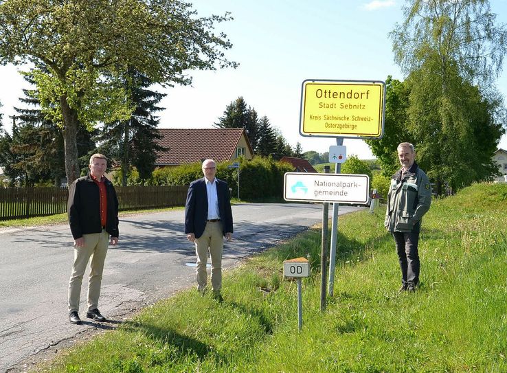 Mit Abstand große Freude: v.l.n.r: Dominique Weidensdörfer, Ortsvorsteher Ortsteil Ottendorf, Mike Ruckh, Oberbürgermeister der Großen Kreisstadt Sebnitz und Dr. Dietrich Butter, Leiter der Nationalparkverwaltung dokumentieren mit den nun montierten Zusatzschildern an den Ortseingängen die Partnerschaft zwischen Ottendorf und der Nationalparkverwaltung. Foto: Stadtverwaltung Sebnitz