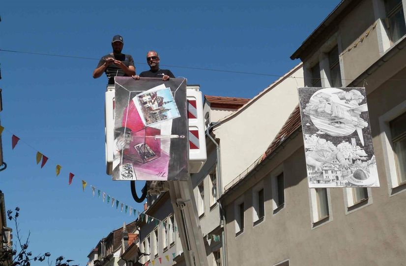 Mitarbeiter des Bauhofes hängen die Bilder der Straßengalerie auf.