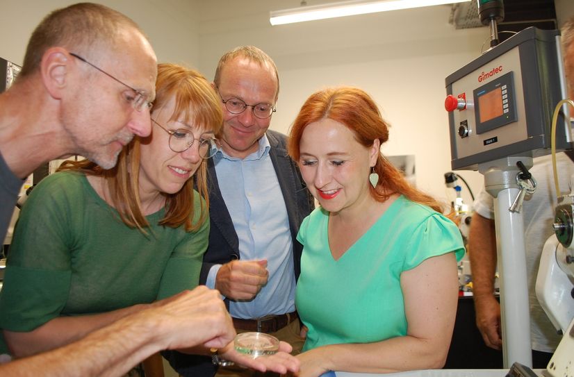 Ein NOMOS-Mitarbeiter zeigt Justizministerin Katja Meier, Energieminister Wolfram Günther und der Landtagsabgeordneten Franziska Schubert (Grüne) (v.l.n.r) Zahnräder für die Herstellung von NOMOS-Uhren.