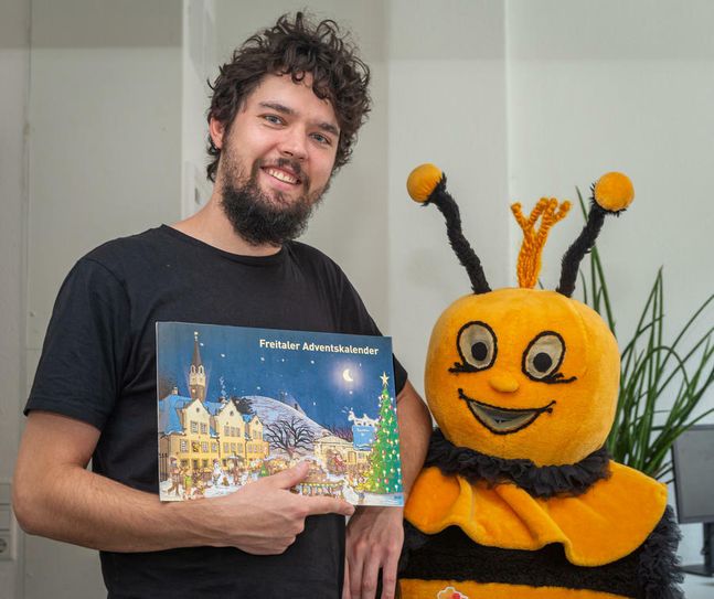 Der Freitaler Musiker und Comic-Zeichner Pascal Bretschneider präsentiert gemeinsam mit Familiencard-Maskottchen Carli den von ihm gestalteten Adventskalender. Foto: Stadt Freital