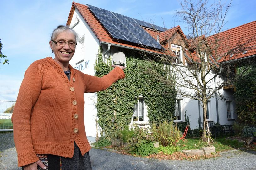 Das Vorstandsmitglied Elke Altmann zeigt auf das Dach des Nebelschützer Gemeindezentrums. Dort steht die erste PV-Anlage der Genossenschaft