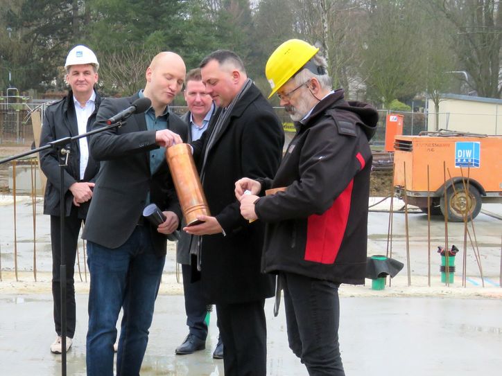 Schulleiter Maik Weinert (2.v.l.) befüllt gemeinsam mit Landrat Udo Witschas (2.v.r) die Zeitkapsel, die wenig später im Grundstein eingelassen wird. 
 Foto: Matthias Stark