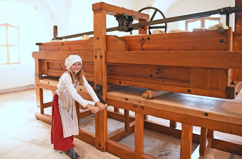 Ferienkinder sind aufgerufen, die historische Wäschemangel selbst zu bedienen, mit selbst mitgebrachten Stoffen oder Wäschestücken.