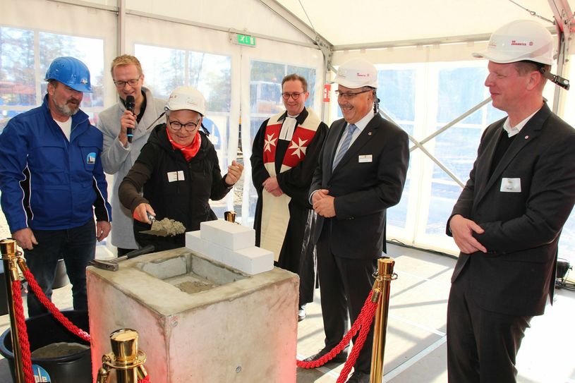 Die Zeitkapsel ist versenkt, jetzt wird sie zugemauert. Die Maurerkelle schwingt hier Renée Ramm (3.v.l.), ehrenamtliche Familienbegleiterin bei den Johannitern. Harald Altekrüger (2.v.r), Landrat Spree-Neiße-Kreis, und Roland Hauke (r.), Projektleiter für das Kinderhaus »Pusteblume«, schauen zu. Ihnen zur Seite stehen Bauleiter Matthias Nicolai (l.) von der Bauunternehmung Böpple GmbH & Co. KG, Moderator Christian Matthée (2.v.l.) und Regionalverbandspfarrer Markus Herrbruck (3.v.r.). Der Würfel mit der Zeitkapsel wird zeitnah im Fundament des Eingangsbereiches des Kinderhauses versenkt. Fotos: Stefan Staindl