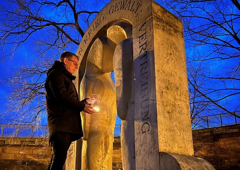Bürgermeister Markus Dreßler entzündet Kerzen am Denkmal für die Opfer von Krieg, Gewalt und Vertreibung.