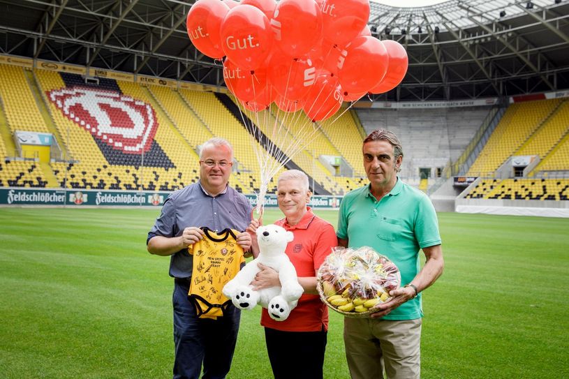 Frank Schröder (Geschäftsführer Event-Agentur Schröder), Andres Rieger (Unternehmenssprecher der Ostsächsischen Sparkasse Dresden) und Ralf Minge (Sportgeschäftsführer der SG Dynamo Dresden) mit den signierten Stramplern und dem Eisbären der Ostsächsischen Sparkasse für Pascal Testroets Tochter Emilia. Foto: Michael Schmidt
