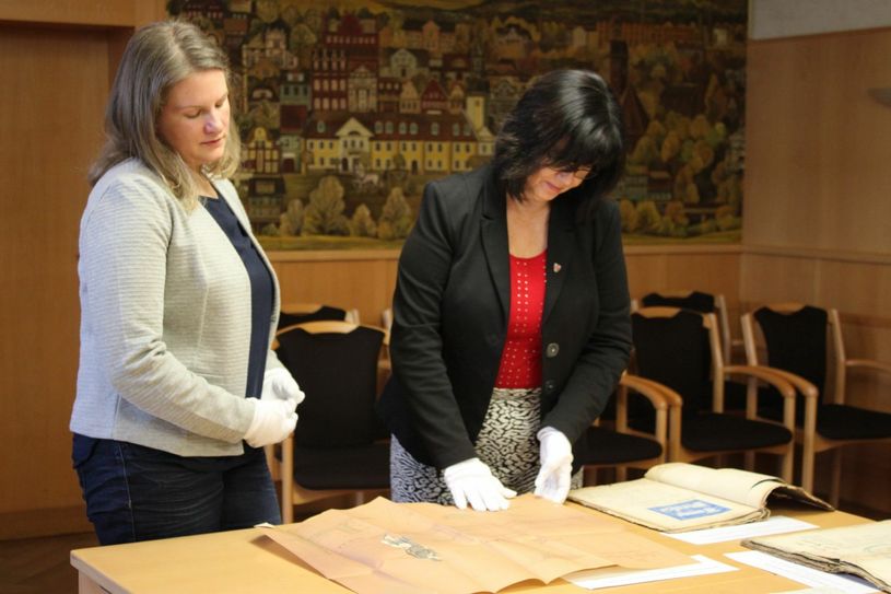 Stadtarchivarin Stephanie Tonke und Bürgermeisterin Christine Hernstier begutachten gemeinsam eine historische Akte mit Entwürfen über das Streichen und Signieren von Straßenschildern aus dem Jahr 1869. Foto: agu