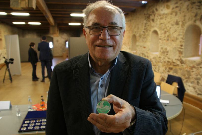 Dr. Rudolf Reimann präsentiert die Medaille: Die Riesaer Festmedaille zeigt das heutige Stadtbild prägende Bauten. Alles überragend steht die Kirche St. Marien, am Riesaer Kloster. Auf der Rückseite wird das anstehenden Stadtjubiläum »900 Jahre Riesa« dargestellt. Der historische Ursprung der Stadt, das Kloster wird so mit der vorbeifließenden Elbe und der Legende zur Entstehung der Stadt verbunden: Ein sich ausruhender Riese reinigt seinen Stiefel vom Sand der Elbe und erzeugt damit einen Hügel, auf dem dann die spätere Stadt Riesa entstanden sein soll. Fotos: Farrar