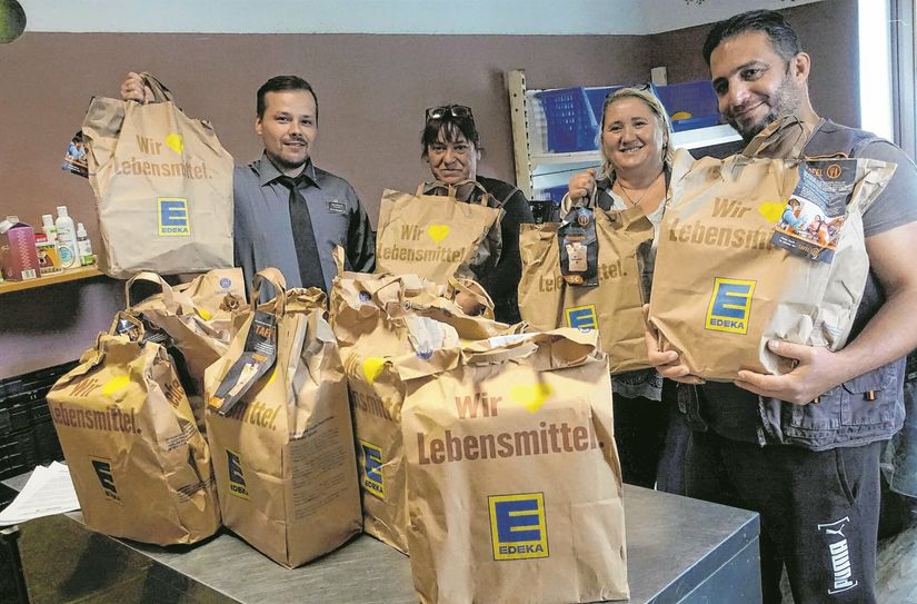 Stefan Gensch (Marktleiter EDEKA Scheunenhofcenter), Silke Kößling (Tafel), Susanne Paul (GF Dem. Frauenbund) und Ali (v.l.n.r.) stehen mit gefüllten Einkaufstüten in der Pirnaer Tafel.