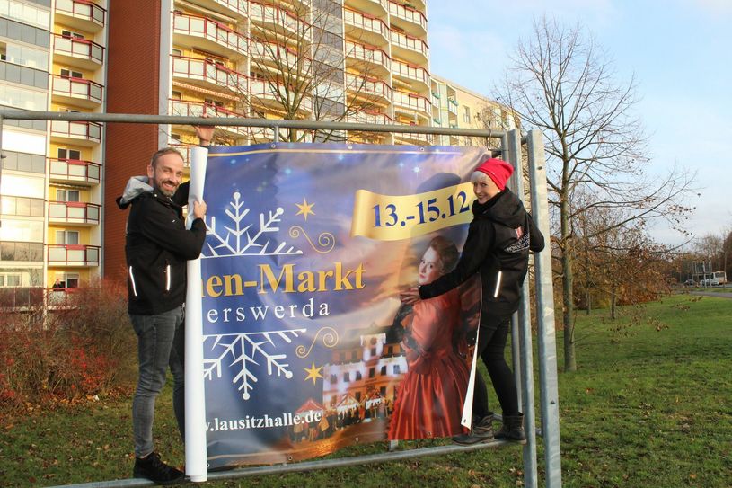 Auch diese Arbeit gehört zur Organisation des Weihnachtsmarktes. In der vergangenen Woche brachten Nico Thäle und Anja Hillmann von der Lausitzhalle das Banner für den Teschenmarkt an. Foto: Silke Richter