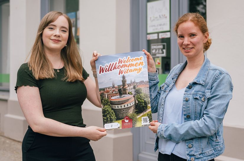 Hanna Maiwald (links) von der Europastadt GörlitzZgorzelec GmbH (EGZ) und Friederike Seifert vom Görlitz für Familie e.V. zeigen eines der neuen, dreisprachigen Plakate, die auf die mehrsprachige Informationsplattform www.welcome-goerlitz-zgorzelec.com verweisen.
