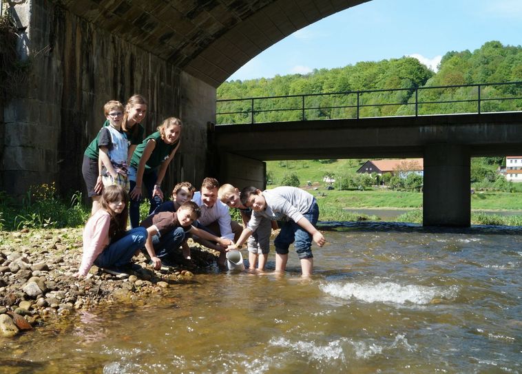 Bürgermeister Tobias Kummer hat sich extra die Königsteiner Junior Ranger zur Hilfe geholt, um Wasser aus der Biela für die Taufe des schicken Doppelstockzuges am kommenden Sonnabend zu schöpfen. Zusammen mit Judith Walz und Daniela Baker von der Nationalparkverwaltung ließen sie sich weder von Brennnesseln oder nassen Füßen abhalten, damit das Wasser in den Krug kommt und das Foto gut gelingt.