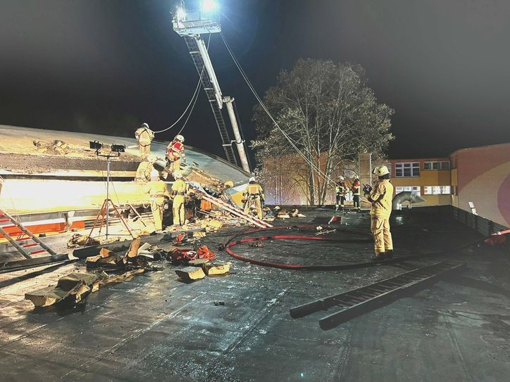 Kameraden der Freiwilligen Feuerwehr sind dabei, an den brennenden Dachstuhl zu kommen.