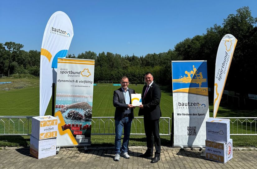 Landrat Udo Witschas (r.) übergibt auf dem Sportforum des SC Thonberg den Fördermittelbescheid an Kreissportbund-Präsident Torsten Pfuhl.