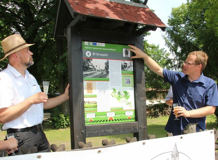 Der Burger Amtsdirektor Tobias Hentschel (li.) und Philipp Seemann (re.) von der Interessengemeinschaft (IG) Spreewaldbahn an der Schautafel, die auf dem Vereinsgelände der IG in Straupitz steht. Foto: sts