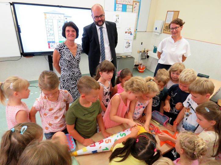 Klassenlehrerin Simone Müller, Staatsminister Christian Piwarz und Schulleiterin Heike Peter (v.l.n.r.) sehen beim Auspacken der vom Minister mitgebrachten Zuckertüte zu. Die Jungen und Mädchen der Klasse 1a freuen sich über das Geschenk.
 Foto: Matthias Stark