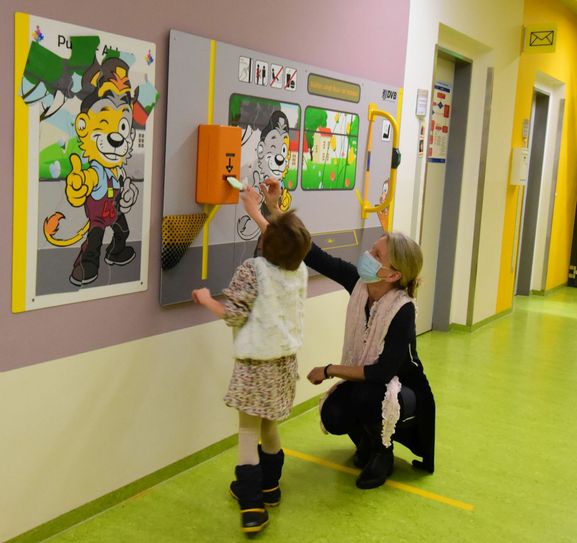 Dr. Katja Albertowski, Leiterin der Autismus-Ambulanz, zeigt Mathilda (6) den originalen Fahrkartenentwerter, den das DVB-Team auf  der Spieltafel montiert hat. Foto: Uniklinikum / H. Ostermeyer