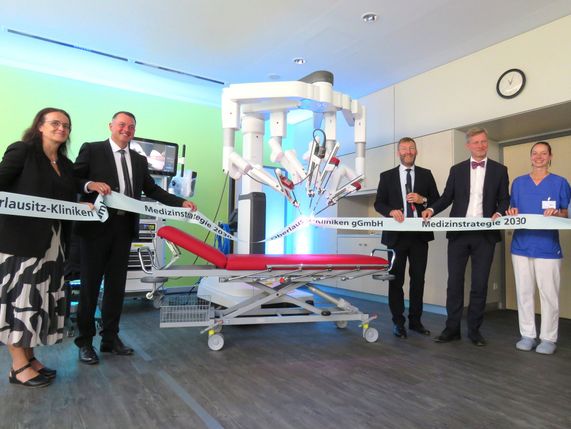 Der neue OP-Roboter da Vinci beim symbolischen Durchschnitt des Bandes, welches von Staatssekretärin Dagmar Neukirch, Landrat Udo Witschas, Klinik-Greschäftsführer Jörg Scharfenberg, Staatskanzleichef Dr. Andreas Handschuh und der OP-Schwester Lisa Winter gehalten wird (v.l.n.r.).