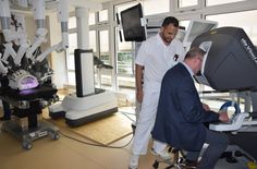 Oberarzt Ahmed Huzaifa leitet Besucher bei der Benutzung des OP-Roboters an. An der Steuerkonsole (rechts im Bild) können die Roboterarme (links) bedient werden.