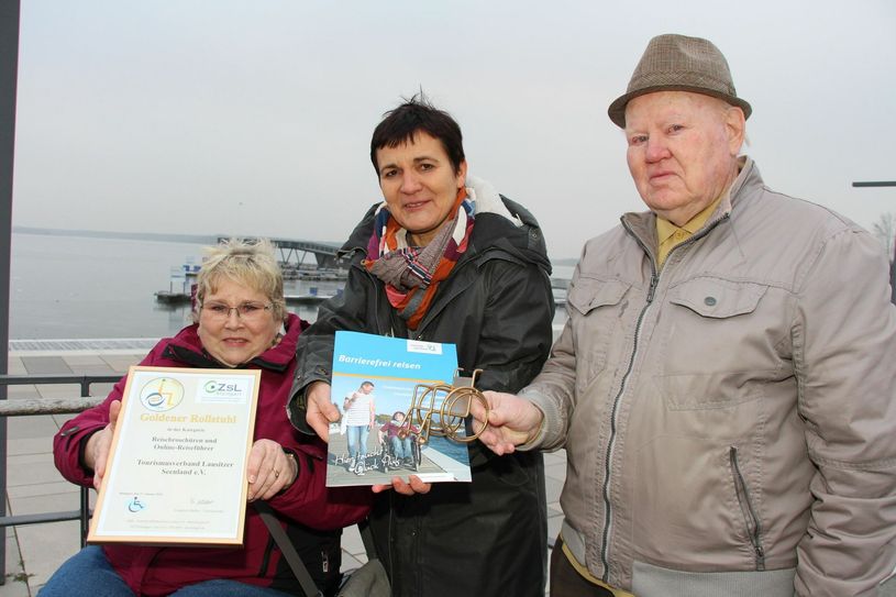 Den »Goldenen Rollstuhl« gab es für die Broschüre »Lausitzer Seenland - Barrierefrei reisen« des Tourismusverbandes Lausitzer Seenland e.V.. Kathrin Winkler (Mitte), Geschäftsführerin Tourismusverband Lausitzer Seenland e.V., Manfred Müller (re.), Blinden- und Sehbehinderten Verband Brandenburg e.V. Bezirksgruppe Senftenberg, und Marei Tuppatsch (li.), Mitglied der Arbeitsgruppe Barrierefrei des Tourismusverbandes Lausitzer Seenland e.V. und Urlaubstesterin für die Broschüre, präsentieren Broschüre, Urkunde und den Goldenen Rollstuhl. Foto: sts